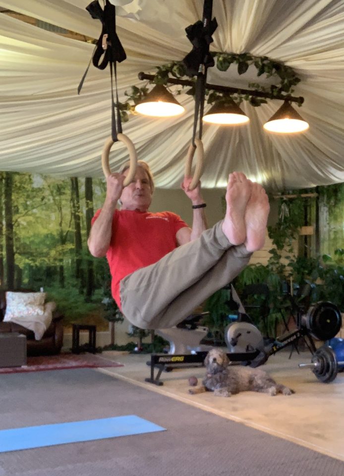 senior man hanging from gymnastic rings in home gym