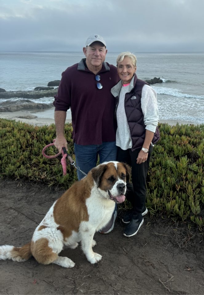 Man and woman with dog near a scenic coastline.