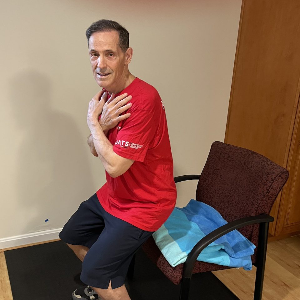 man in red Senior Planet shirt performing chair-assisted squat
