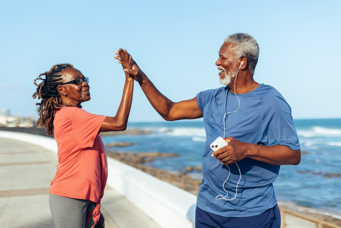 Senior couple celebrating fitness achievements with a high five by the seaside. Active and happy elderly exercising outdoors by the ocean.