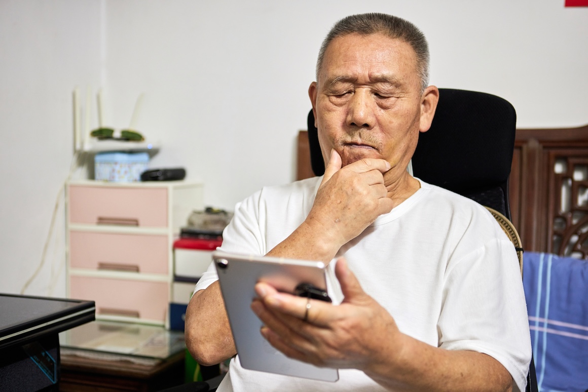 senior Chinese man anxiously looking at tablet computer in living room